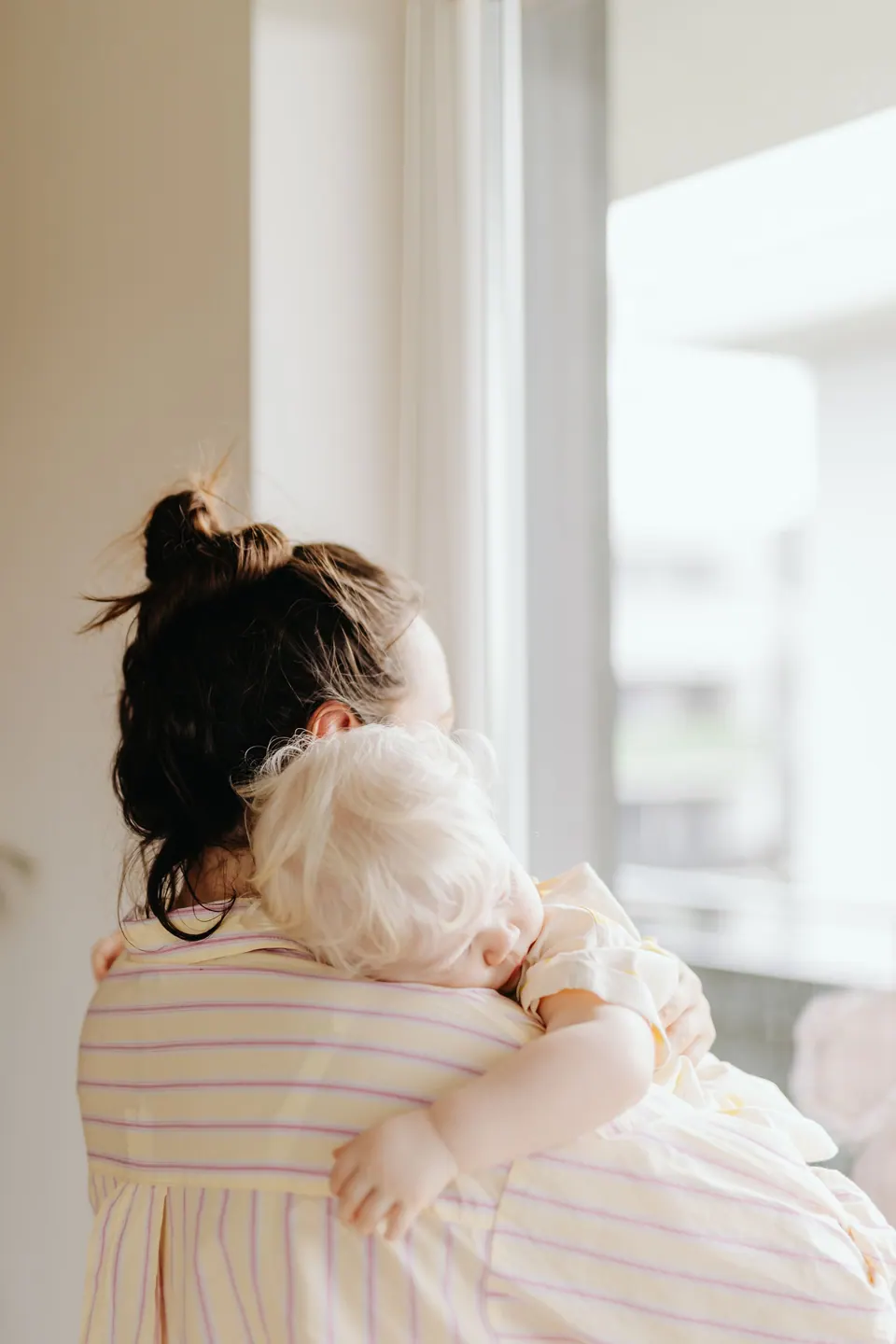 Mama su kūdikiu ant rankų žiūri pro langą